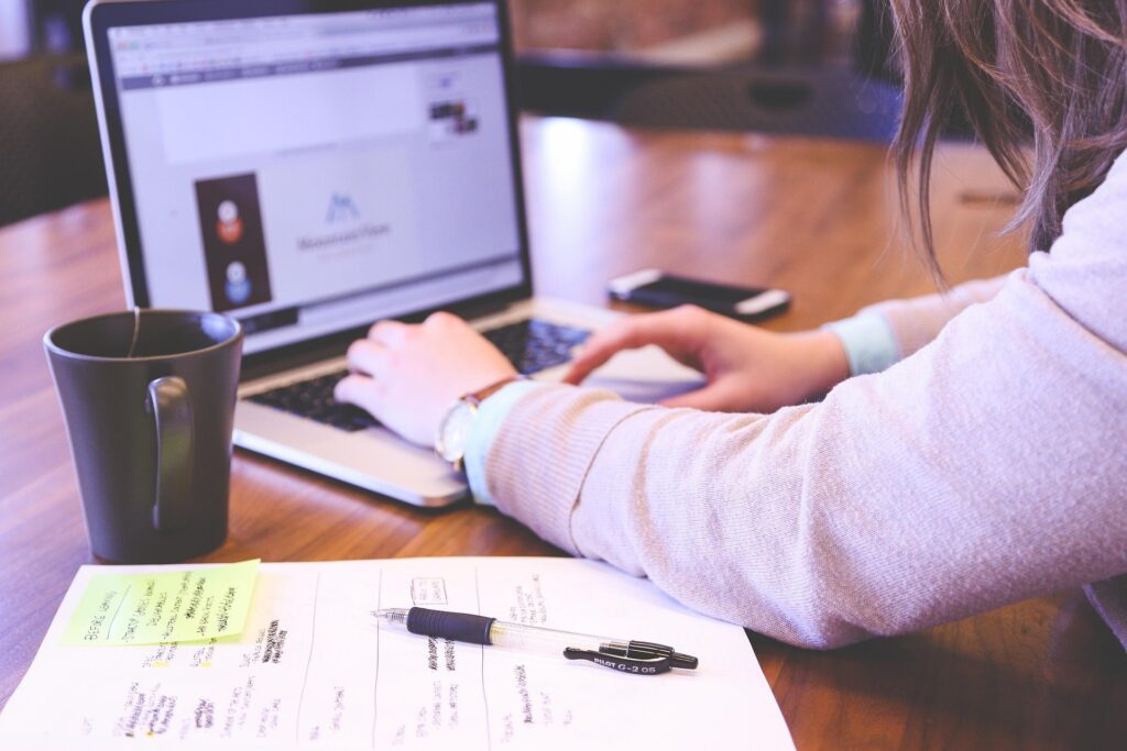 Personne tapant sur un ordinateur portable, notes manuscrites et stylo sur un bureau en bois, gestion des factures